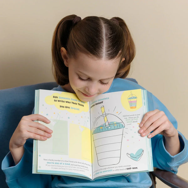 A young girl smiling while looking at an open InClouds Journal for kids. The interactive page features prompts for positive self-thoughts and affirmations, showcasing the journal as a powerful mindfulness tool for building children's self-love.