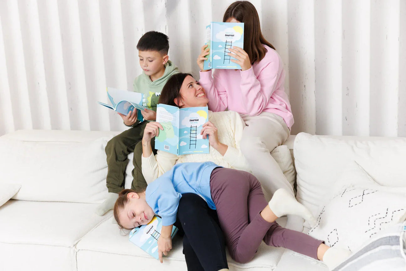 A happy mother and four children relaxing on a white sofa, each holding an InClouds Journal for kids. This cozy family moment illustrates using gratitude journals to promote mindfulness and emotional intelligence in children at home.