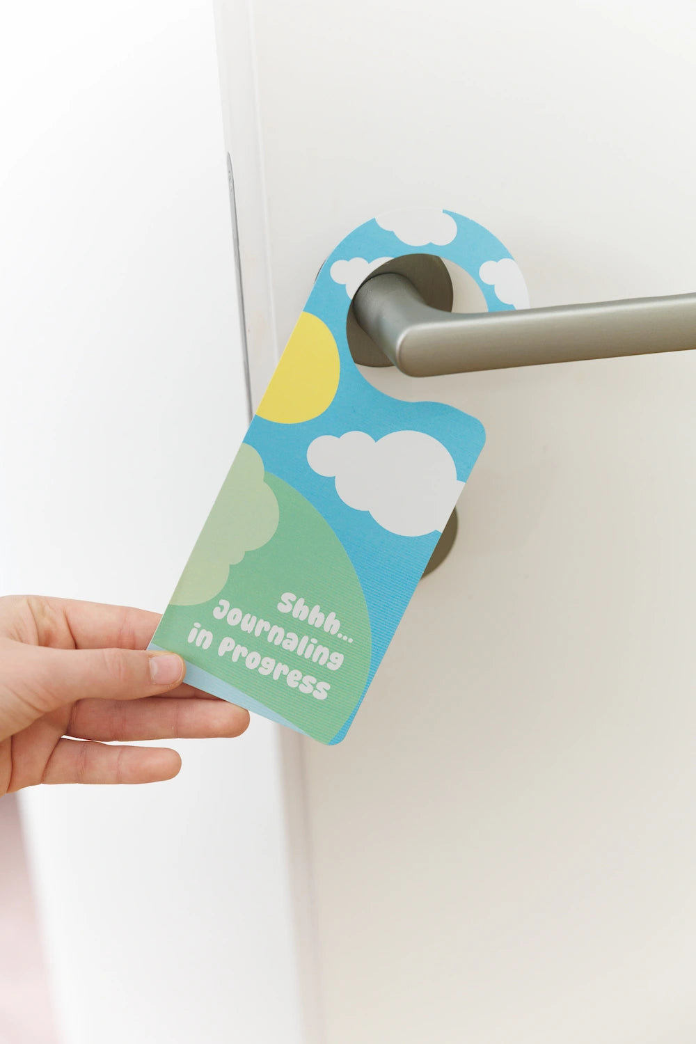 Door hanger with a cloud and sun design held by a hand against a white background