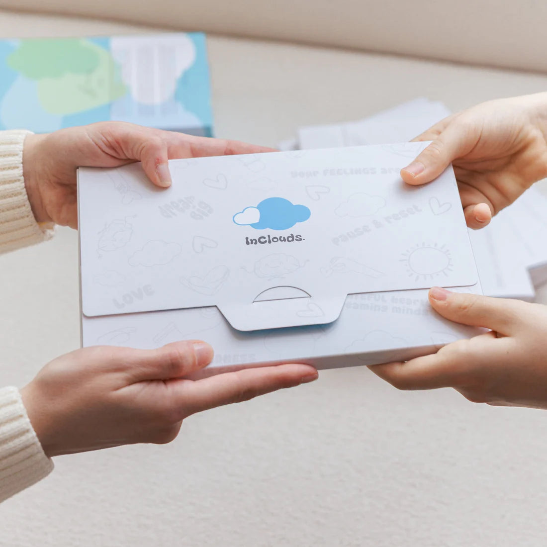 Two hands holding an InClouds Journal gift box with the cloud logo, showcasing the branded packaging experience