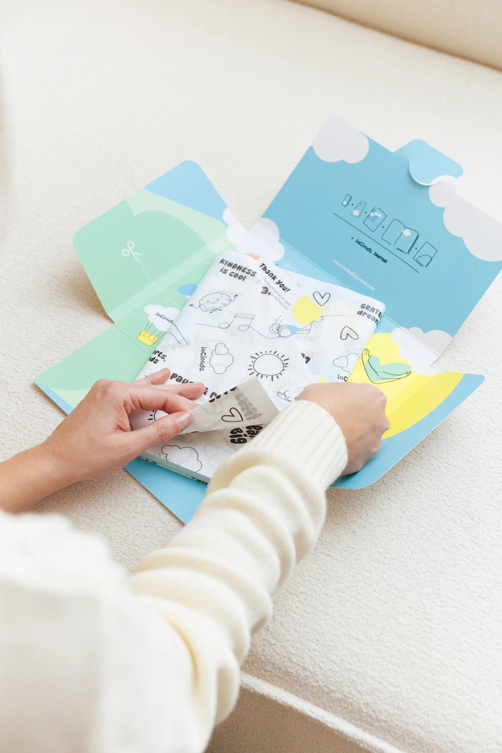 Hands opening a beautifully wrapped InClouds. Journal featuring branded tissue paper and a custom blue mailer box.