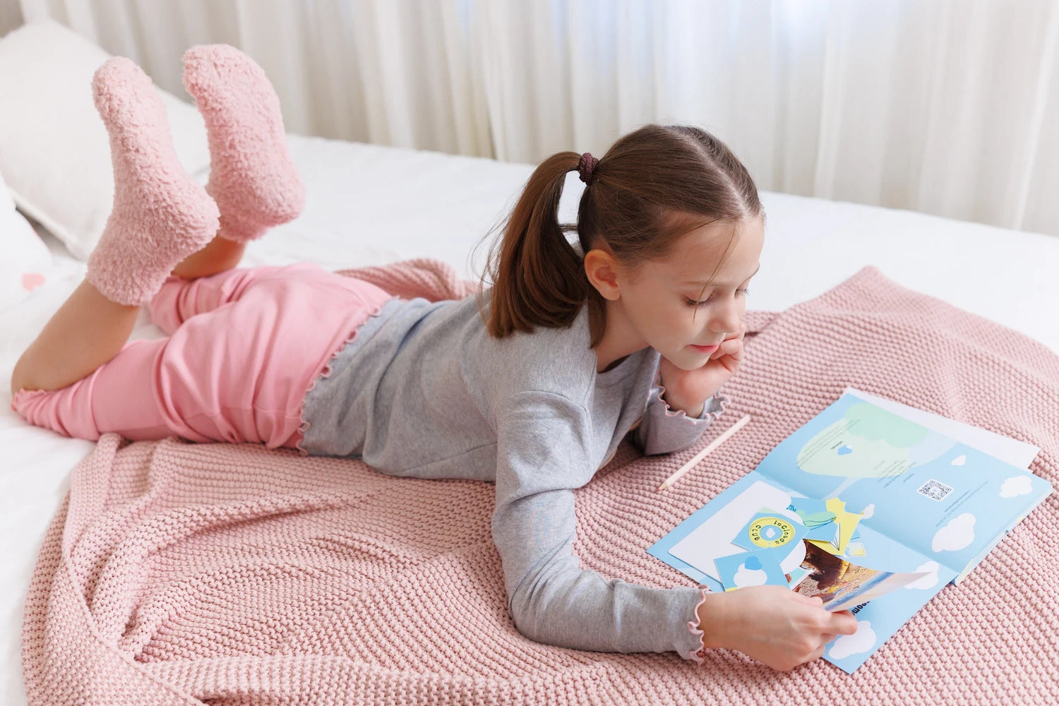 Young girl lying on a bed, creatively decorating her InClouds. Journal for kids with stickers and photos.