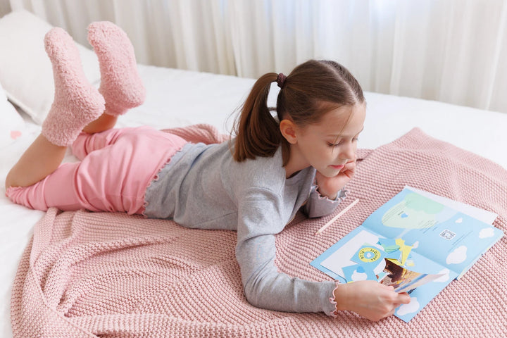 Young girl lying on a bed, creatively decorating her InClouds. Journal for kids with stickers and photos.